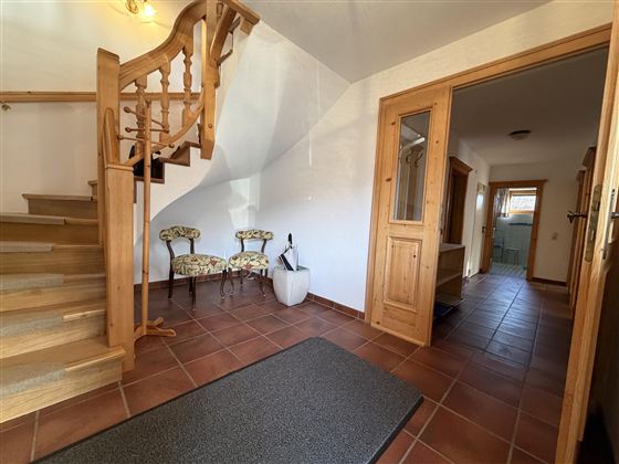 Ein einladender Flur mit einer Holztreppe und zwei Stühlen. Der Raum ist hell erleuchtet und hat braune Fliesen.