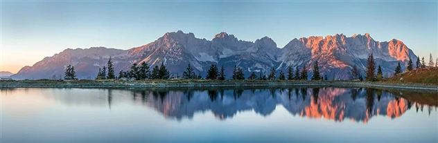 A majestic mountain landscape is reflected in a tranquil lake. The colors of the sunrise illuminate the peaks and create a peaceful atmosphere.
