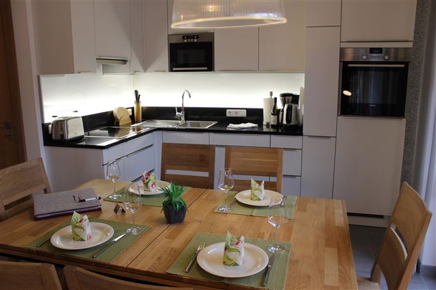 Eine moderne Küchenzeile mit minimalistischen Designs und einer hellen Beleuchtung. Der Esstisch ist hübsch gedeckt mit Tellern und frischen Servietten.