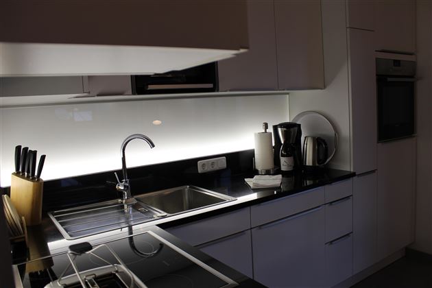 Eine moderne Küche mit schwarzen Arbeitsflächen und weißen Schränken. Es gibt einen Wasserhahn, Küchengeräte und eine elegante Beleuchtung.