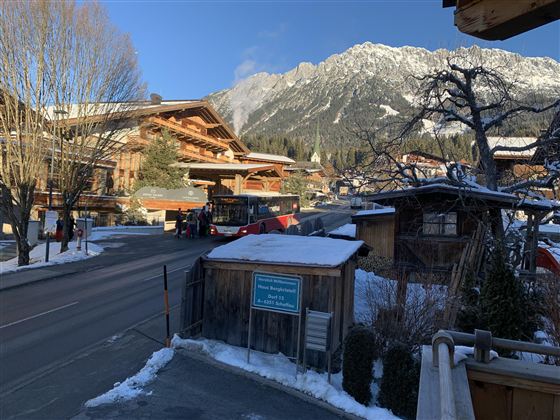 Een besneeuwd berglandschap met traditionele houten huizen. Een bus stopt langs de weg voor de bergen.