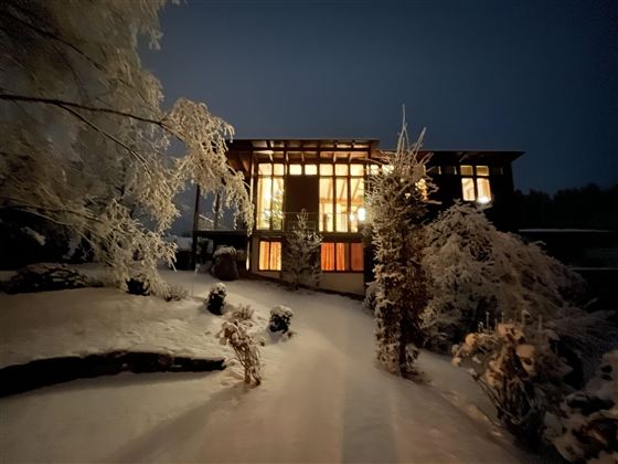 Ein modernes Haus im Schnee bei Nacht, beleuchtet von warmem Licht. Der Garten ist mit schneebedeckten Bäumen geschmückt.