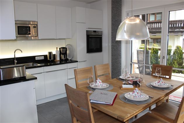 Een moderne keuken met een houten eettafel en elegant servies. De witte kasten en het zwarte aanrecht zorgen voor een stijlvolle uitstraling.