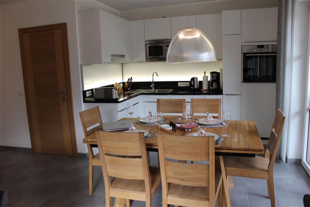 Een moderne keuken met een eetgedeelte van hout. De ruimte is helder en uitnodigend, met keukenapparatuur en een groot raam.