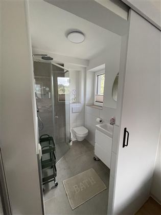 Een moderne badkamer met douche, toilet en wastafel. De muren zijn licht en er is een groot raam voor natuurlijk licht.