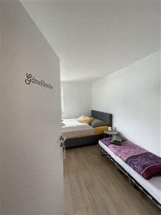 Een lichte kamer met twee bedden en eenvoudige inrichting. Er is een smalle ruimte met een houten vloer en eenvoudige decoratie.