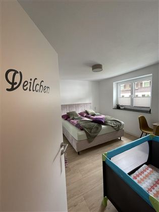 Een moderne slaapkamer met een tweepersoonsbed en een kinderkamer. Er zijn grote ramen die voor veel daglicht zorgen.