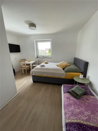 Een lichte kamer met een groot bed en een gezellige zithoek. Er is een tafel en een bank, evenals een televisie aan de muur.