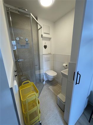 Een moderne badkamer met een doorzichtige douche en een toilet. Gele opbergmanden staan in de ruimte.