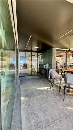 Moderní vstupní prostor se skleněnými dveřmi. V pozadí jsou vidět stoly a židle.