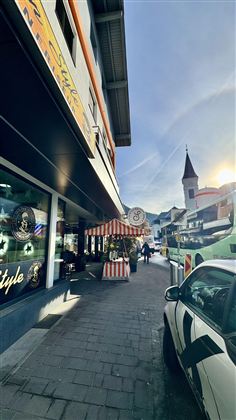 Rušná ulice s barevnými obchody a stanem. V pozadí je vidět kostelní věž.