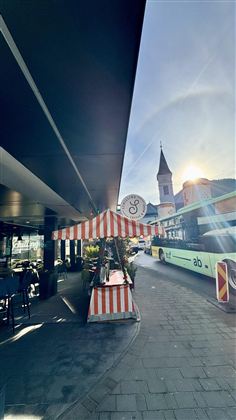 Rušná ulice. V pozadí je vidět autobus a kostelní věž, zatímco vychází slunce.