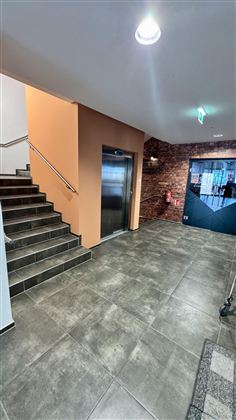 Moderní schodiště se schody a výtahem. Stěny jsou v neutrálních barvách a je zde barevný akcent.