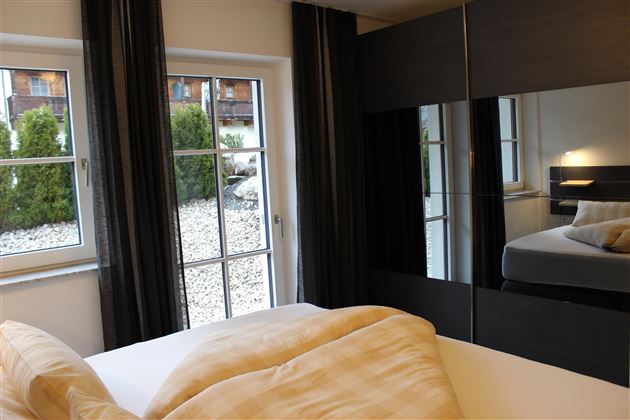 Een modern ingerichte slaapkamer met grote ramen en een kast. De kamer heeft lichte kleuren en voelt uitnodigend aan.