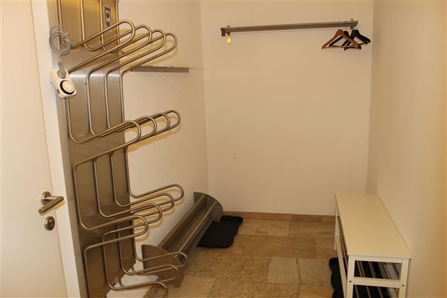 Ein leeres Raum mit einer Kleiderablage und einem Haken. Die Wände sind weiß, und der Boden besteht aus Fliesen.