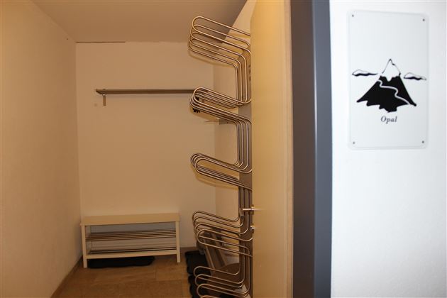 Een eenvoudige ruimte met een kledingrek en een bank. Aan de muur hangt een bord met een bergmotief.