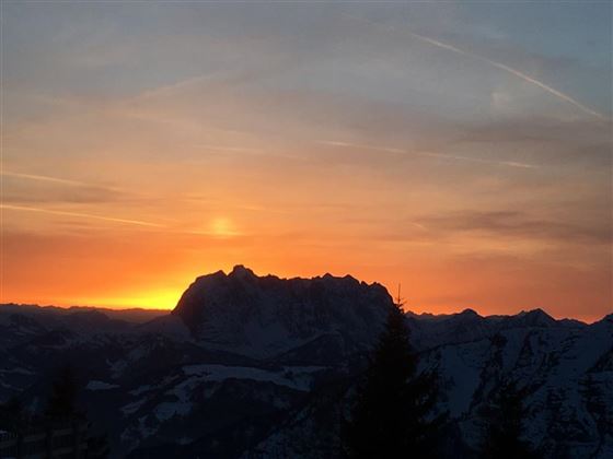 A beautiful sunset over snow-covered mountains. The orange and red hues of the sky exude a calm atmosphere.