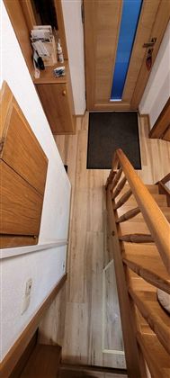 A hallway with a wooden staircase and a green entrance area. The walls are light, and the door has a blue window.