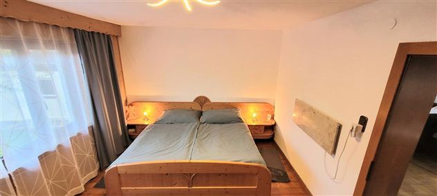 A cozy bedroom with a double bed and wooden details. Soft lighting creates a relaxed atmosphere.