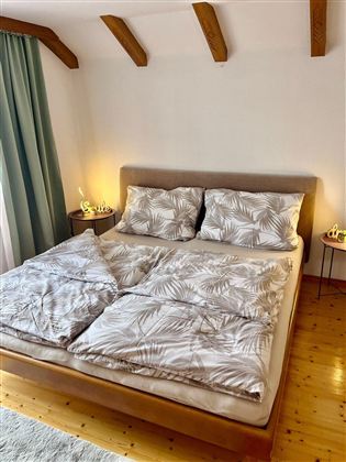 A cozy bedroom with a large bed and bedding in leaf design. There is soft light and a calm atmosphere.