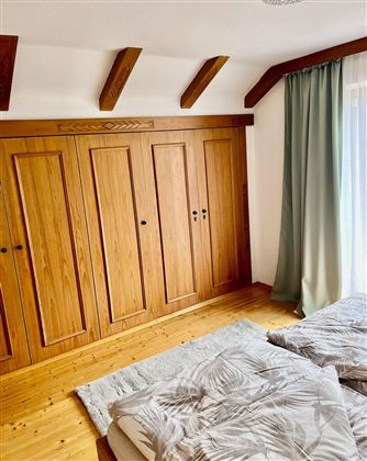 A modern bedroom with an elegant wooden wardrobe and two sleeping mattresses. The room is bright and friendly, with a large window and a soft curtain.