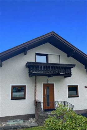 A cozy house with a balcony and a modern entrance area. The sky is clear and blue.