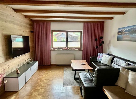 A cozy living room with wooden paneling and a large window. The room design is modern with a comfortable couch and a television.