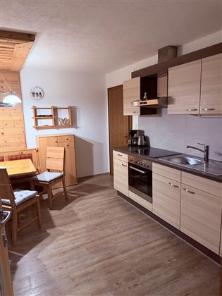 A modern kitchen with light wooden cabinets and a cozy dining table corner. The equipment includes a stove, a sink, and a coffee machine.