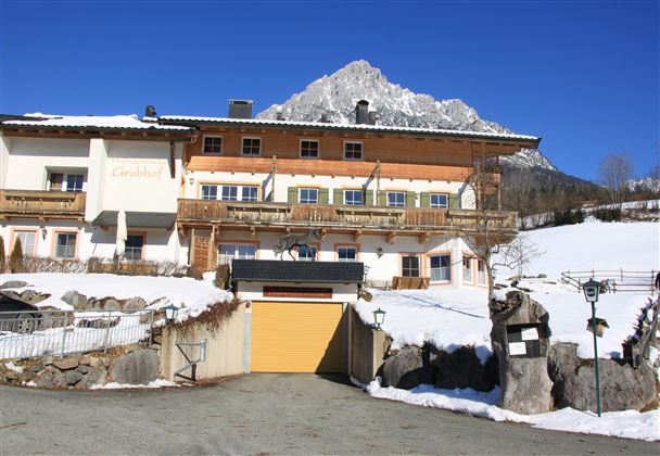 A picturesque building with several balconies, surrounded by snow-covered landscapes. In the background, a high mountain rises under a clear blue sky.