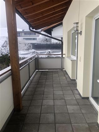 Ein geräumiger Balkon mit einem Dachüberstand und hellen Fliesen. Im Hintergrund sind schneebedeckte Landschaften zu sehen.