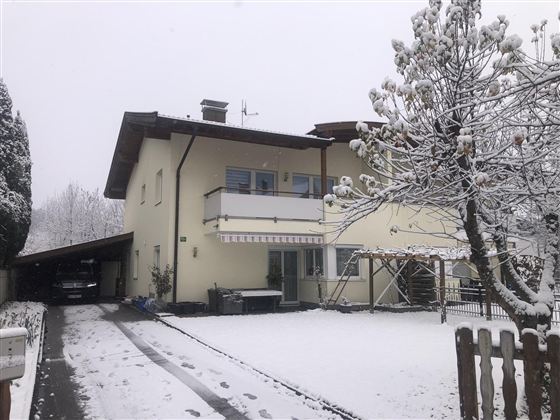Ein Haus im Schnee mit einem gemütlichen Carport. Der Garten ist mit frischem Schnee bedeckt und es ist bewölkt.