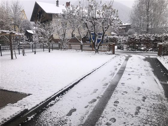 Eine verschneite Winterlandschaft mit Spuren im Schnee. Im Hintergrund sind Bäume und ein Haus sichtbar.