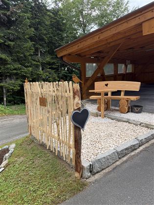 A beautiful entrance area with a wooden railing and a wooden bench. The ground is covered with pebbles and there is a lot of greenery in the surroundings.