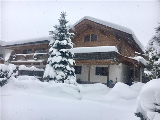 Ein schönes Holzhaus inmitten von tiefem Schnee. Hohe verschneite Tannenbäume umgeben das Gebäude.