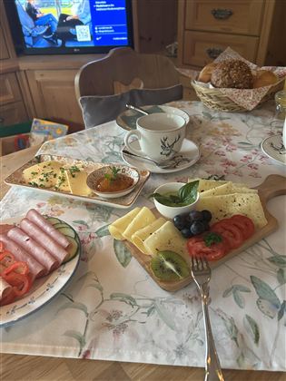 Ein gedeckter Tisch mit verschiedenen Frühstücksleckereien. Darauf sind Käse, Schinken, Tomaten und eine Tasse Kaffee zu sehen.