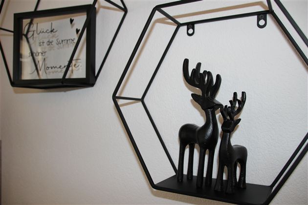 Eine dekorative Wand mit schwarzen Geweihstatuen und einem eingerahmten Schriftzug. Die Statuen stehen in einem hexagonalen Regal und verleihen dem Raum einen modernen Touch.