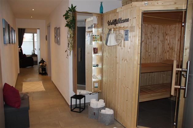 Ein heller Flur mit dem Saunabereich aus Holz. Auf der linken Seite befinden sich gemütliche Sitze und dekorative Elemente.