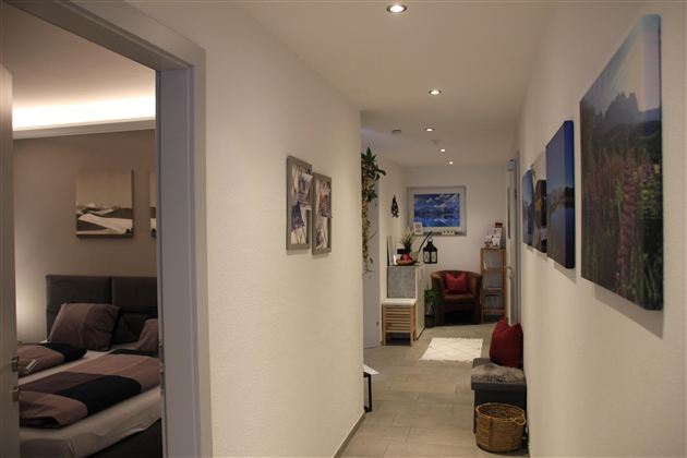 Ein heller Flur mit modernen Bildern an der Wand. Auf der linken Seite ist ein Schlafzimmer sichtbar, der Raum wirkt einladend und gemütlich.