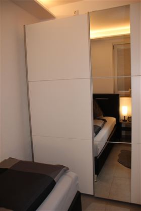 Das kleine Schlafzimer ist ausgestattet mit einem weißen Kleiderschrank mit Spiegel.