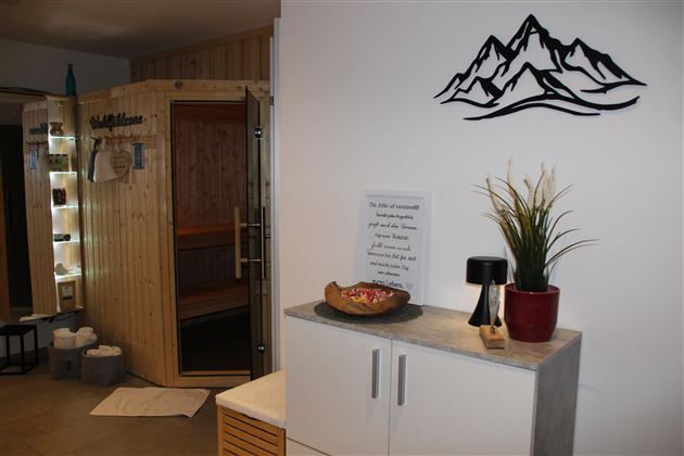 Ein gemütlicher Wellnessbereich mit einer Holzsauna und einem modernen Dekor. Pflanzen und dekorative Elemente verleihen dem Raum eine entspannende Atmosphäre.