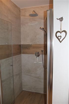 Eine große Duschkabine mit neutralen Fliesen. Der Raum wirkt hell und einladend.