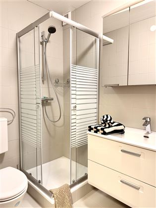 A modern bathroom with a glass shower and a white sink. On the sink lies a striped towel and the walls are brightly tiled.