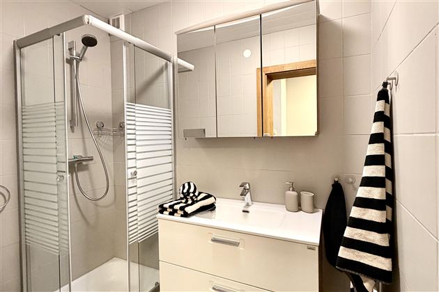 A modern bathroom with a shower and a sink. The decor is bright and minimalist, featuring a large mirror and striped towels.