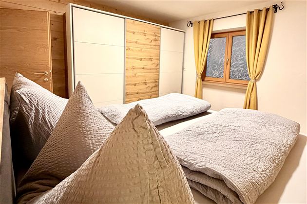 A cozy bedroom with two beds and large pillows. The walls are made of wood, and the window has yellow curtains.