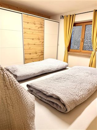 A cozy bedroom with two single beds and a window. The yellow curtains give the room a friendly atmosphere.