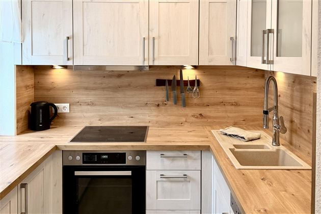 A modern kitchen with wooden paneling and white cabinets. It features cooktops, an oven, and a sink.