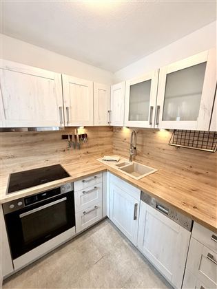 A modern kitchen with white cabinets and a wooden countertop. It is well-equipped with appliances and a spacious sink.