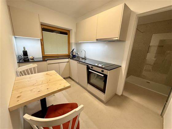 Eine moderne Küche mit hellen Schränken und einem Essbereich. Es gibt einen Ofen, eine Spüle und ein Fenster, das Tageslicht hereinlässt.