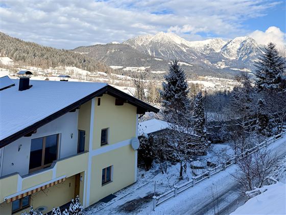 A charming house in a snowy landscape. In the background, majestic mountains and a blue sky are visible.