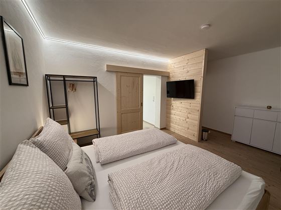 Ein modernes Schlafzimmer mit zwei Betten und geschmackvoller Ausstattung. Es gibt einen Flachbildfernseher und harmonische Holz-Elemente.